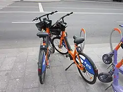 Сравнение электровелосипедов «2.0» исходной (слева) и т.н. «улучшенной» модели (справа). Видны разные замки, разные грипсы и резинка на корзине у «улучшенной» модели справа